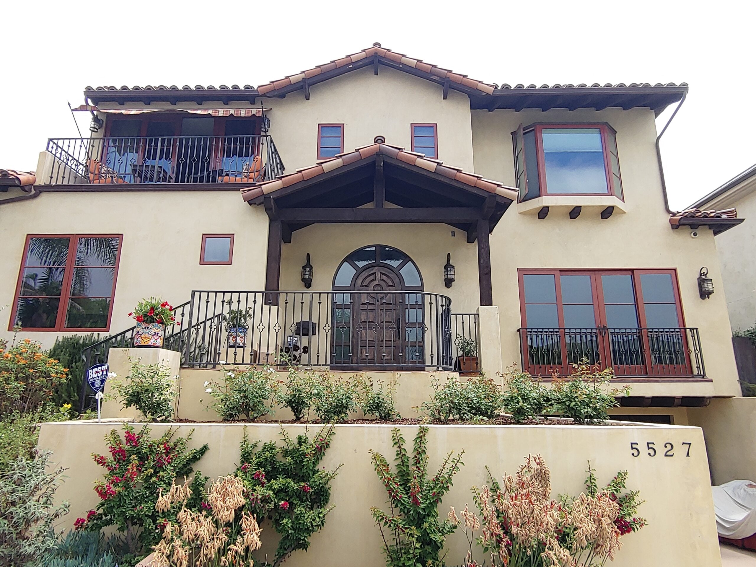 Exterior view of a beige Mediterranean-style home with iron railings and terraced front landscaping.