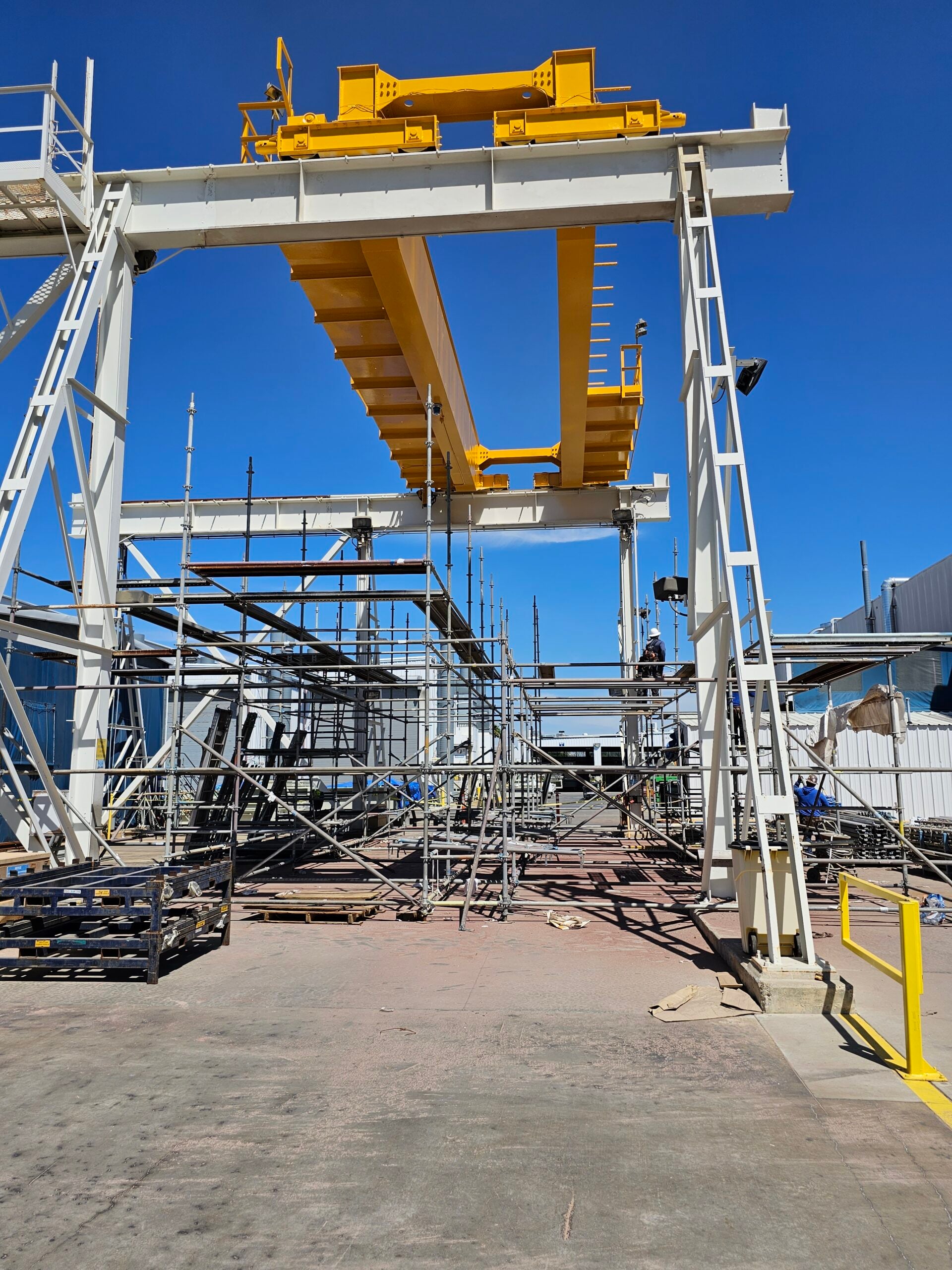 Industrial gantry crane structure under construction or maintenance with metal scaffolding and workers.