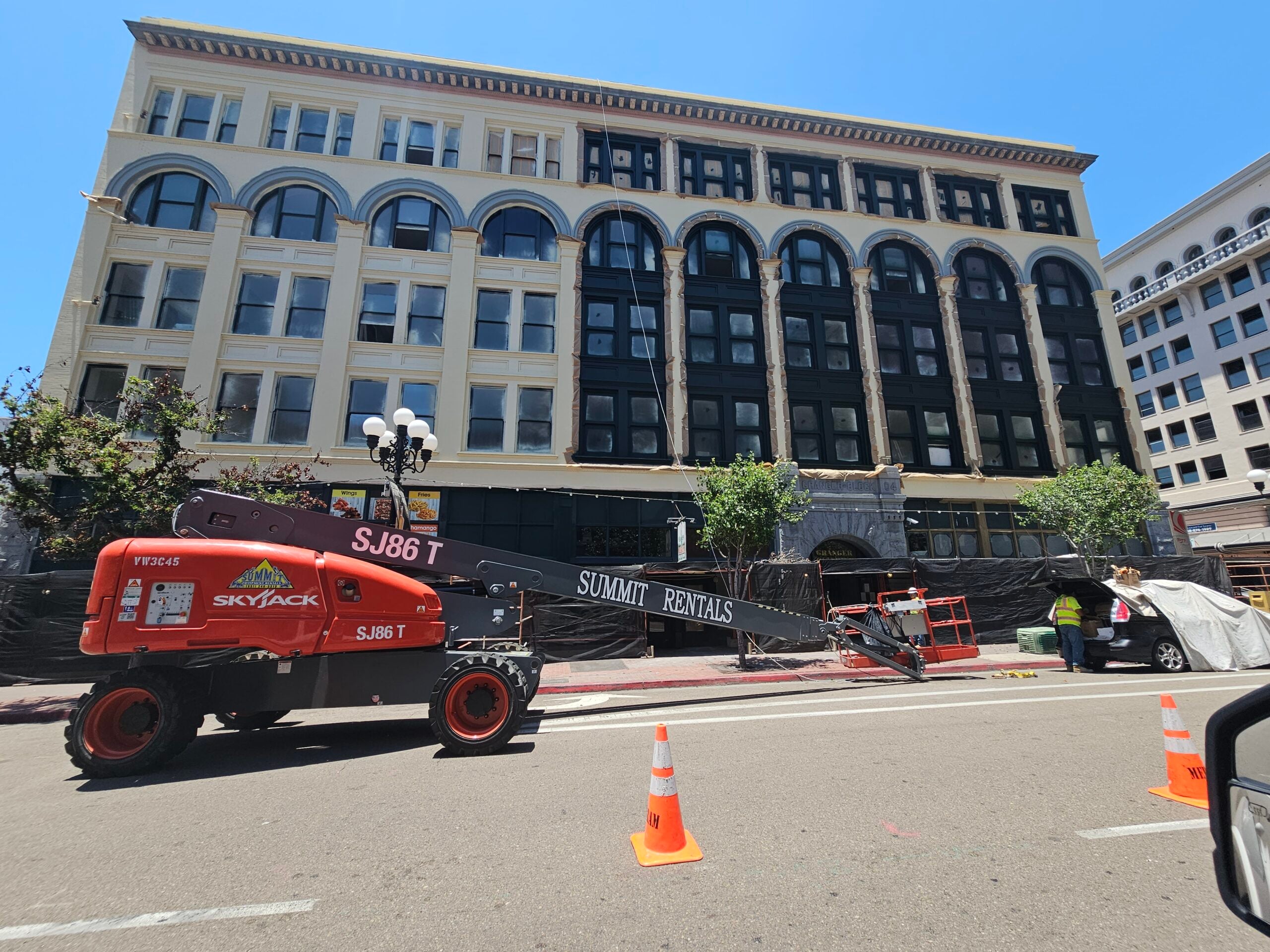 An orange construction boom lift parked on the street during a exterior painting renovation of a historic multi-story building.