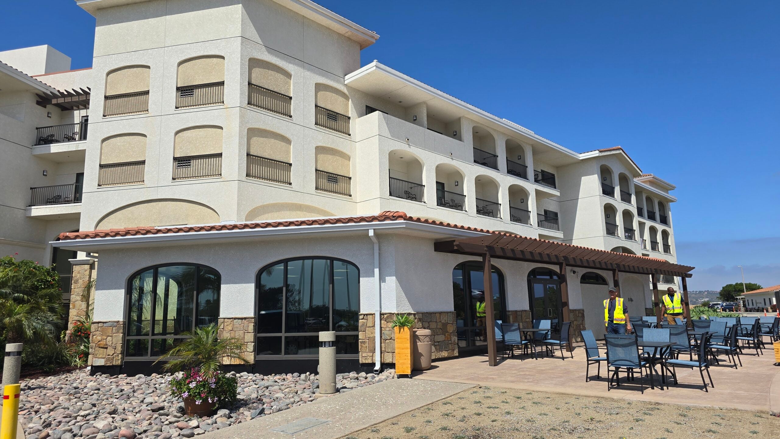 Exterior view of a white multi-story hotel building with an outdoor patio dining area and workers.