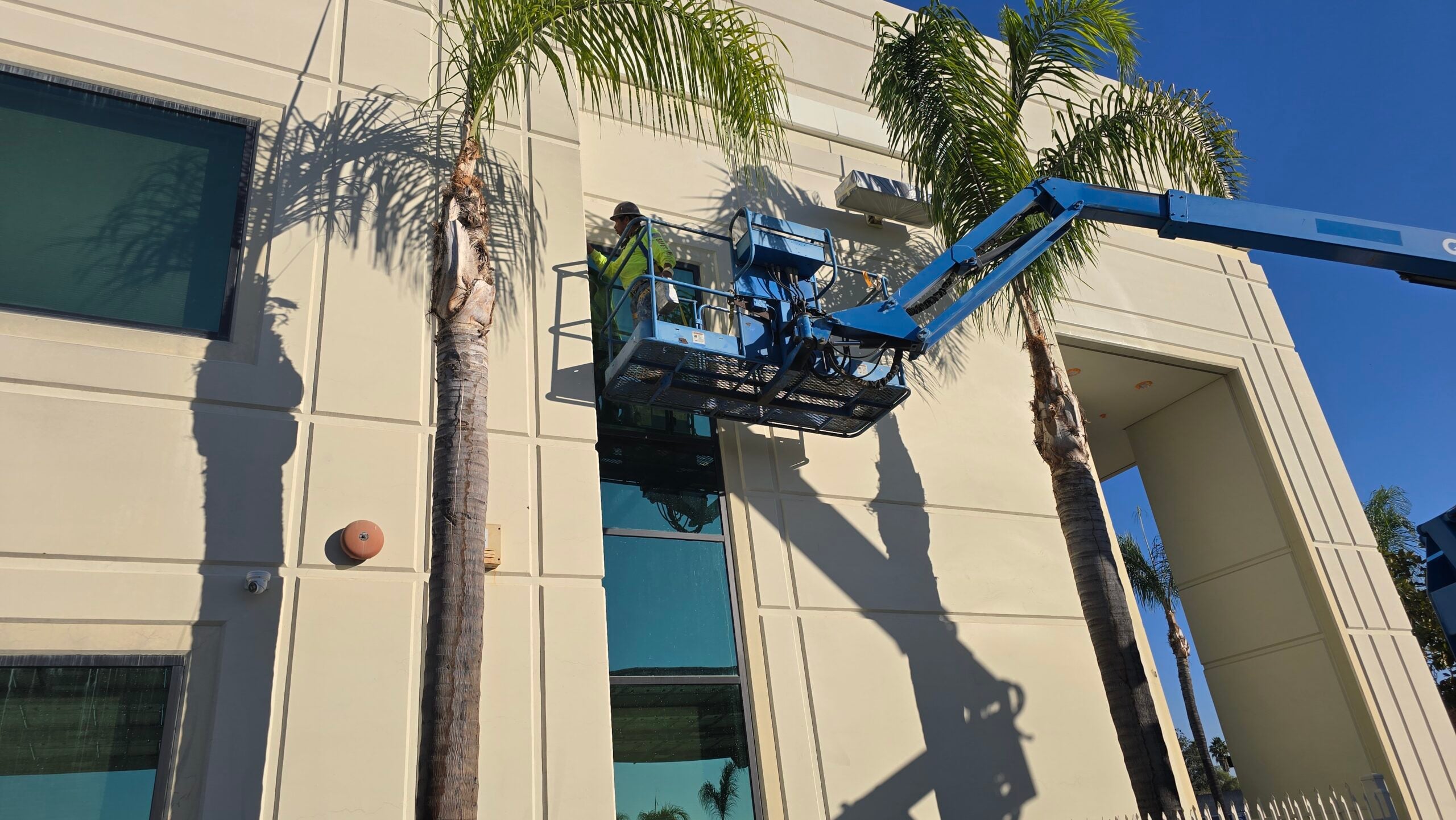 A maintenance worker using a hydraulic lift basket to service a building facade.