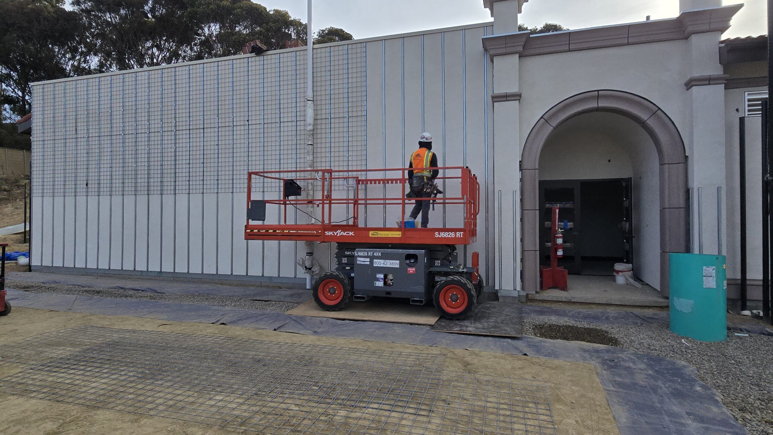 A worker operating a Skyjack scissor lift to install or service panels on a building facade.