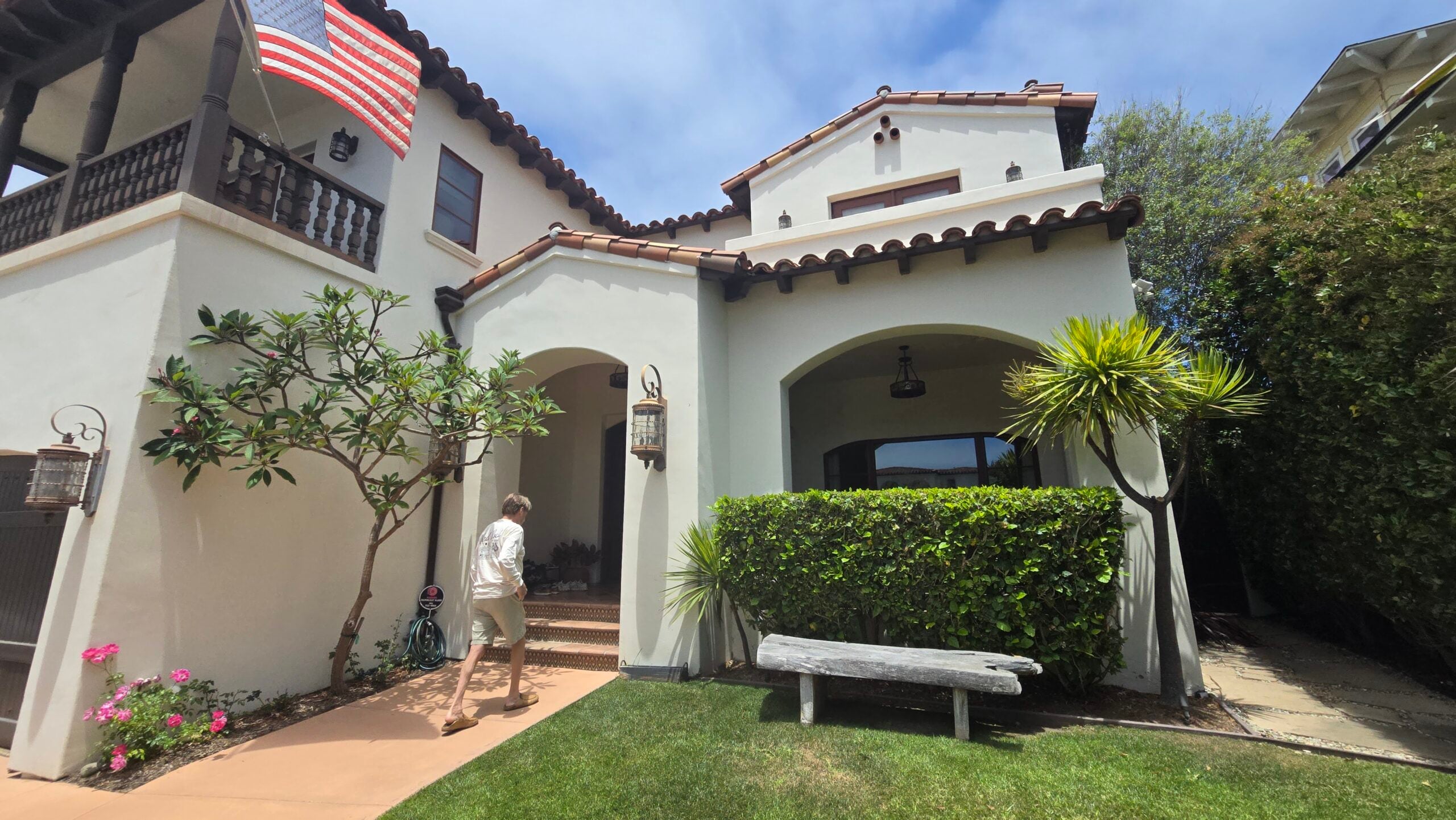 Exterior view of a Spanish-style home with an American flag and a person walking toward the front entrance.