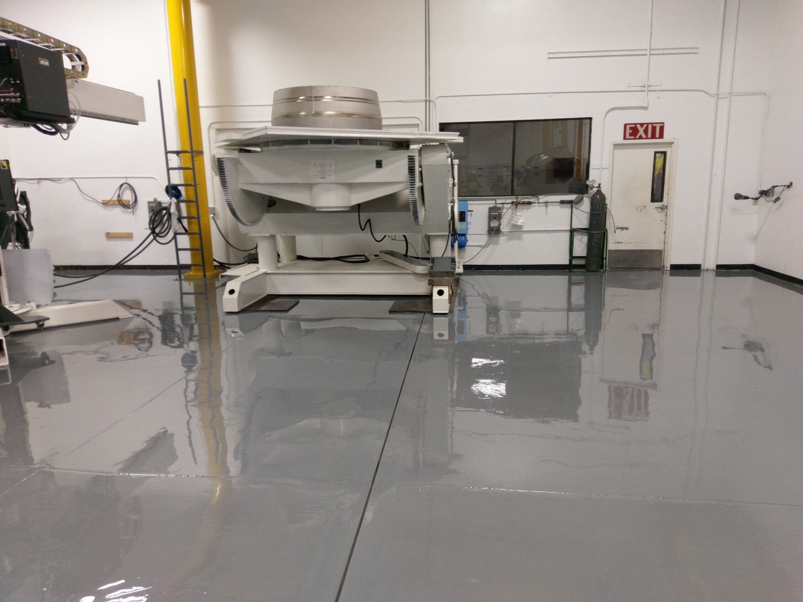 A large white industrial machine stands on a freshly applied, high-gloss grey epoxy floor in a warehouse facility.