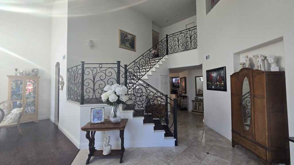 An elegant home foyer showing a grand staircase with decorative iron railings and classic furniture.