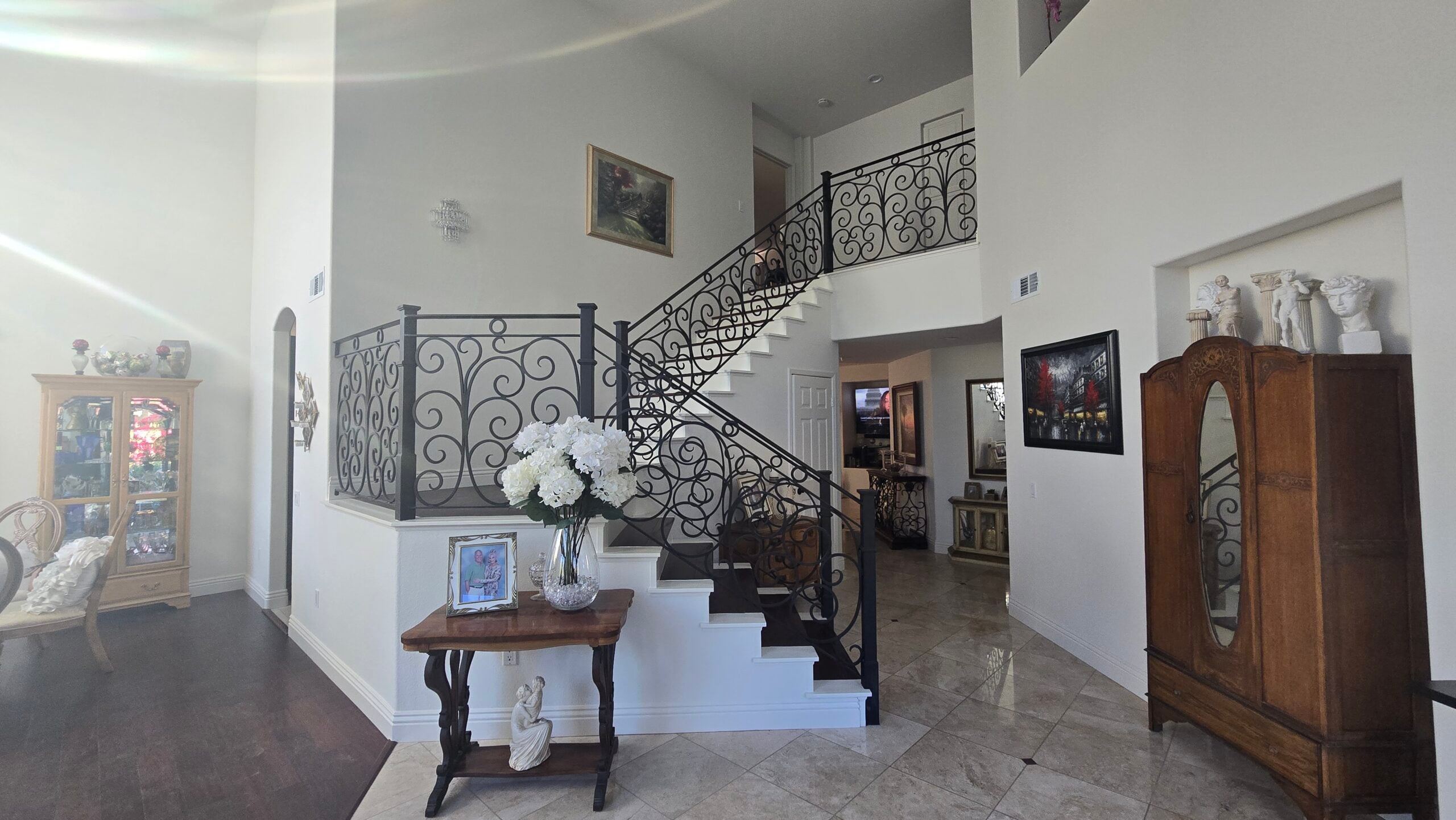 An elegant home foyer showing a grand staircase with decorative iron railings and classic furniture.