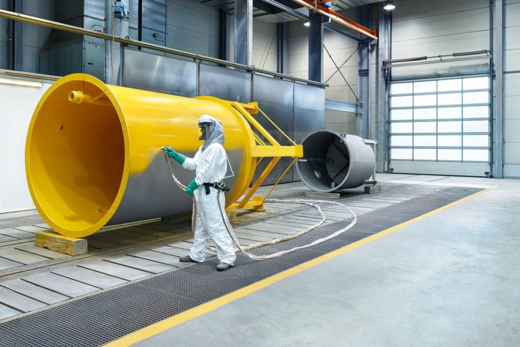Industrial painter spray applying a yellow protective coating to large equipment for a painting company in San Diego, CA.